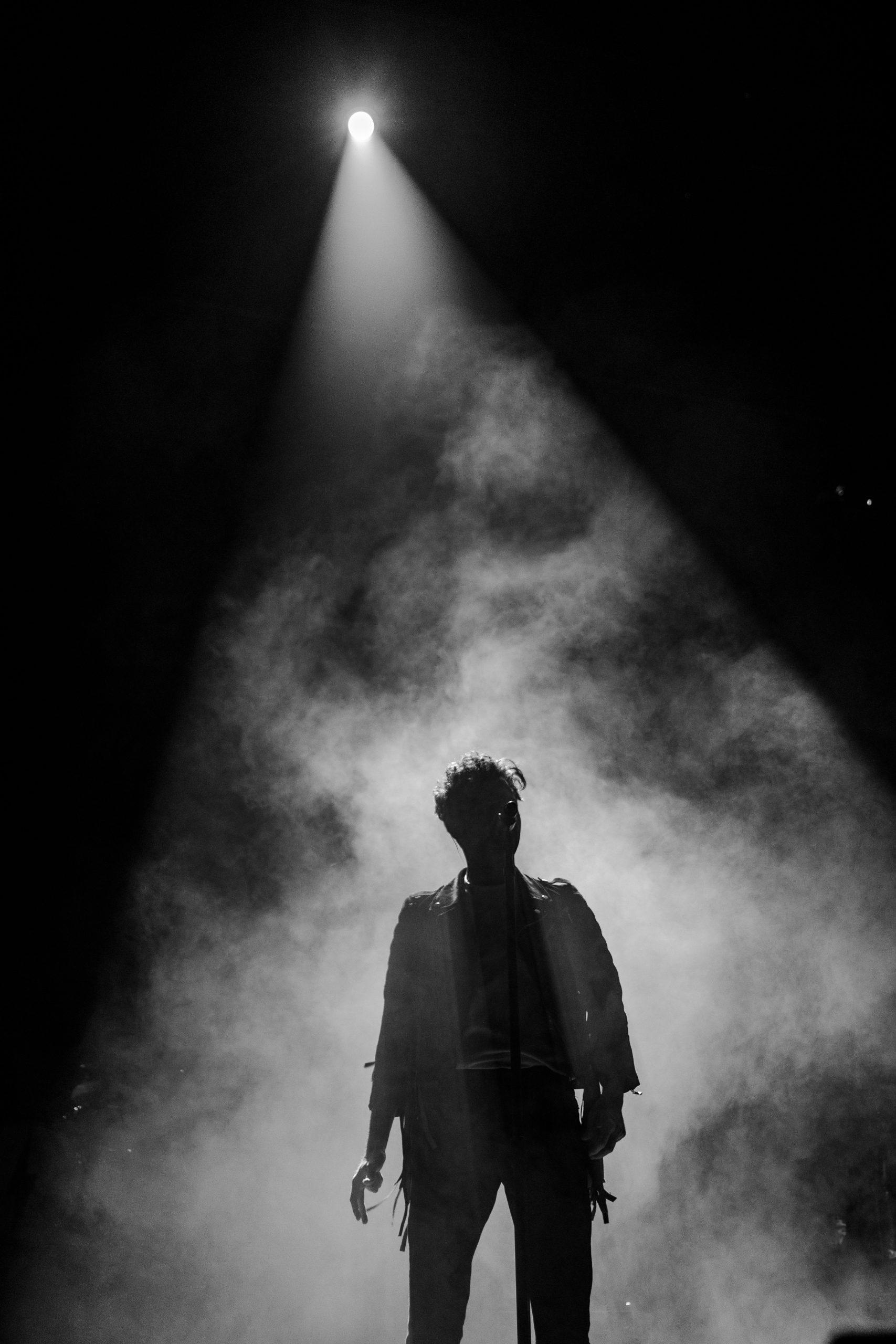 a man standing on stage with fake smoke and a spotlight