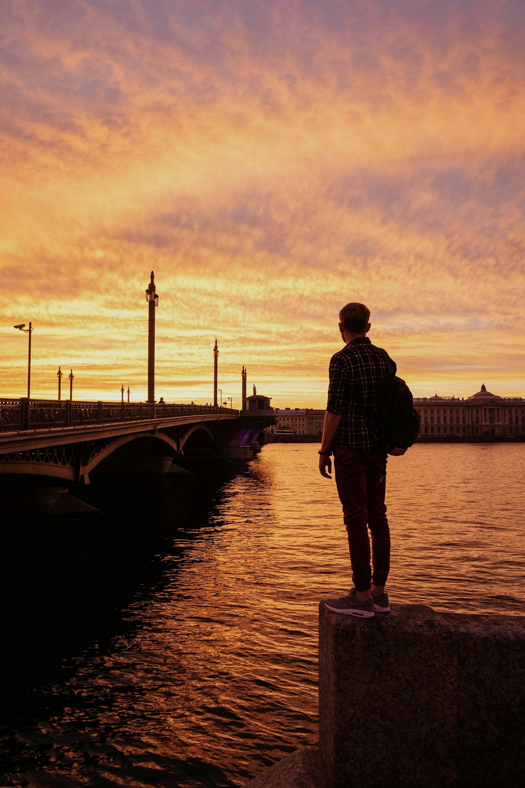 Man standing on a ledge next to water and a bridge